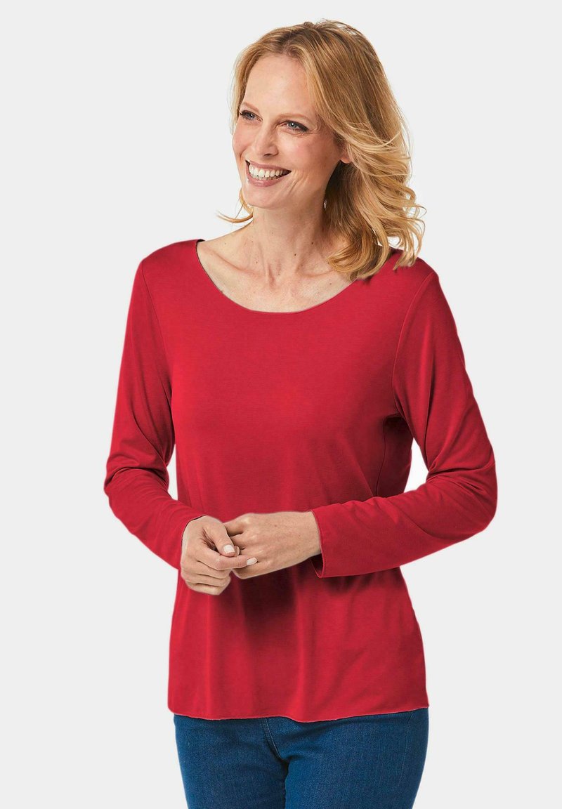 Rotes langärmliges Oberteil mit Rundhalsausschnitt, aus weichem Stoff gefertigt. Das Design hat eine lockere Passform und wird mit blauen Jeans kombiniert.