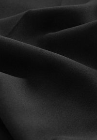 Tissu noir avec une texture lisse et mate, présentant des plis doux et une profondeur subtile dans les plis. Aucun motif visible ni détail de quincaillerie.