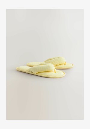 Sárga pamut papucsok, steppelt textúrával, amelyek thong dizájnnal és puha párnázattal rendelkeznek. A forma lekerekített, finom szövésmintával.