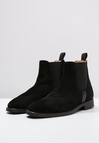 Bottines en suède noir avec des panneaux latéraux élastiques, un bout arrondi et un talon bas empilé ; dotées d'une languette à l'arrière.