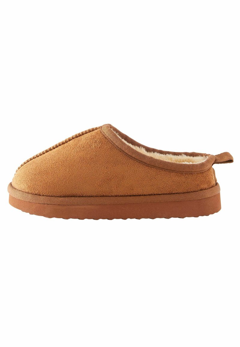 Tan suede slipper met een zachte faux fur voering, laag profiel ontwerp, en een getextureerde rubberen zool. Voorzien van gestikte accenten en een achterste trekband.