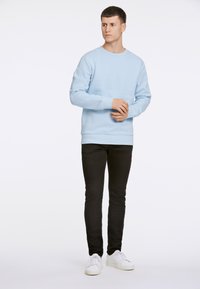 Ljusblå sweatshirt med rund hals, långa ärmar, ribbade muddar och fåll; kombinerad med svarta smala jeans och vita sneakers.