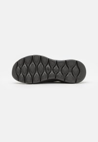 Black rubber shoe sole with a textured pattern and flex grooves for traction. Features raised circular accents and a rounded toe design.
