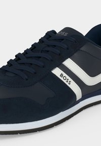 Baskets bleu marine avec bandes blanches sur les côtés, de la marque ""BOSS,"" avec des lacets noirs et une semelle blanche avec semelle extérieure noire.