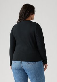 Fekete, hosszú ujjú felső, kerek nyakkivágással, sima anyagból készült, világoskék, magas derekú farmernadrággal párosítva, melyen hátsó zsebek találhatók.
