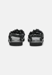 Black slide sandals featuring gathered straps, flat sole, and a smooth finish. The design emphasizes comfort with a minimalist aesthetic.