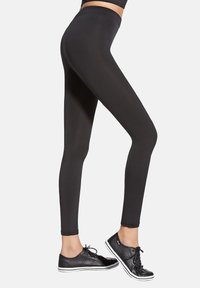 Czarne legginsy o dopasowanym kroju i wysokim pasie, wykonane z elastycznego materiału, zestawione z czarnymi sneakersami z białymi sznurowadłami i podeszwami.