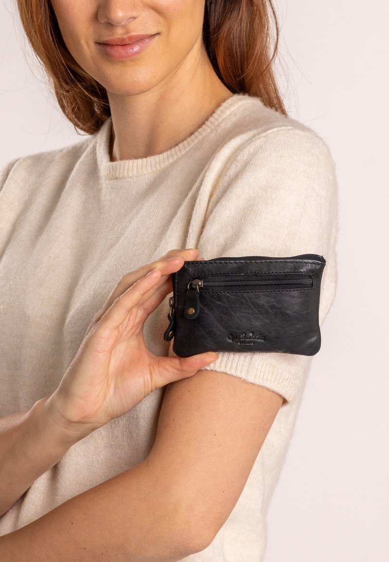 Must mustrikotist lõhe, väike ristkülikukujuline, tekstureeritud pind, millel on logo ja lisakinnitus eesseinas.