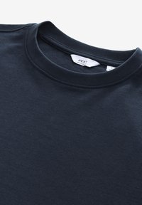 Maglietta in cotone blu navy scuro con scollo rotondo, morbida al tatto e dal design minimalista. Etichetta del brand visibile all'interno del colletto.