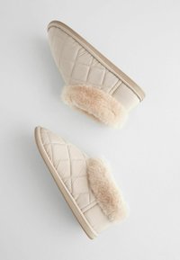 Quiltede beige hjemmesko med en fluffy lysbrun kant. Blødt, syntetisk materiale og en flad, struktureret sål. Et simpelt, moderne design.