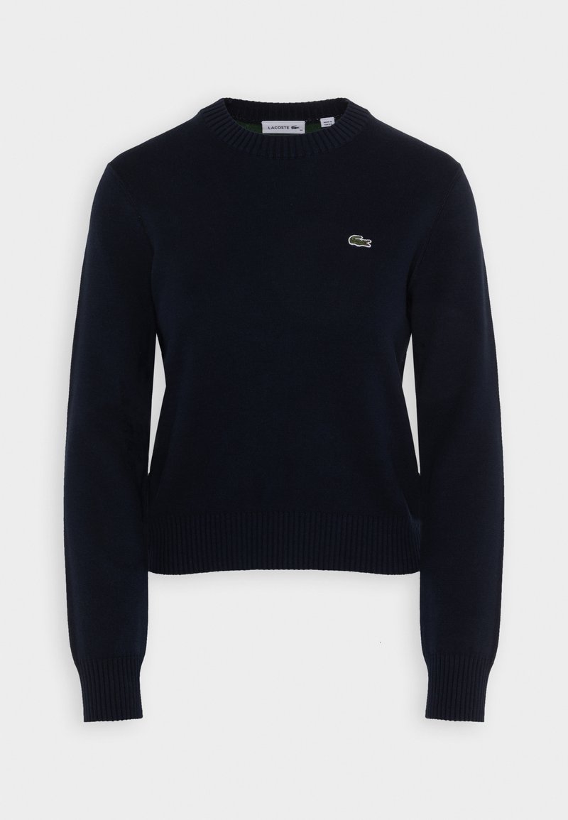 Maglione lavorato a maglia blu navy con scollatura rotonda, polsini e orlo a costine. Presenta un piccolo logo Lacoste verde ricamato sul petto.