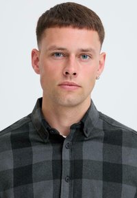 Tamsiai pilka ir juoda langelinė marškinėlių chemise su minkštos tekstūros audiniu. Turi klasikinį apykaklę ir juodus mygtukus.