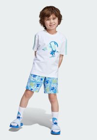 Vit bomulls t-shirt med blå grafik, ljusblå shorts med tropisk tryck, blå sandaler och vita strumpor med grafiska detaljer.