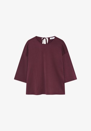 Haut bordeaux en tissu texturé, avec un col rond, des manches trois-quarts et une fermeture à nouer au dos.