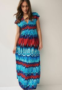 Maxikjole i blå, rød og hvid med tie-dye mønster. Har korte ærmer og en smocket bærestykke for et tætsiddende look. Lang og luftig.