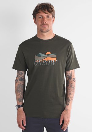 T-shirt en coton vert olive avec un graphique de collines superposées et un soleil en orange et bleu, avec le mot "OXBOW" imprimé en dessous.