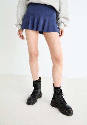 Navy flared mini skirt with a fitted waist and ruffled hem, paired with black lace-up combat boots featuring yellow stitching.