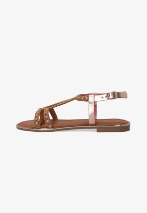 Braune flache Sandalen mit metallischen Akzenten, ausgestattet mit einem T-Strap-Design, das mit kleinen Perlen verziert ist, und einer Schnallenverschluss am Knöchel.