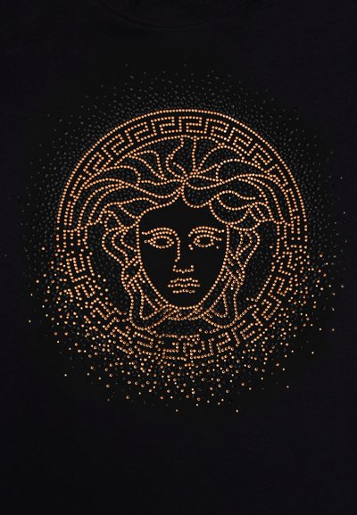 Camiseta negra con un diseño central de Medusa hecho de tachuelas naranjas, con un patrón decorativo de llave griega alrededor del borde.