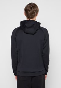 Czarna bluza z kapturem wykonana z fakturowanej tkaniny, z regulowanym kapturem, długimi rękawami i dopasowanym pasem. Prosty i funkcjonalny design.