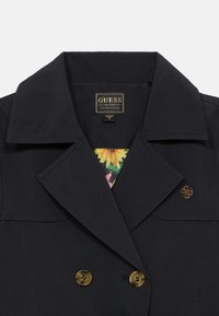 Veste noire croisée en tissu lisse, dotée d'une doublure intérieure à motifs floraux et de boutons dorés.