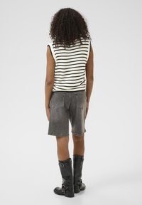 Striped black and white sleeveless top, gray denim shorts, and black knee-high boots with buckles, viewed from the back.