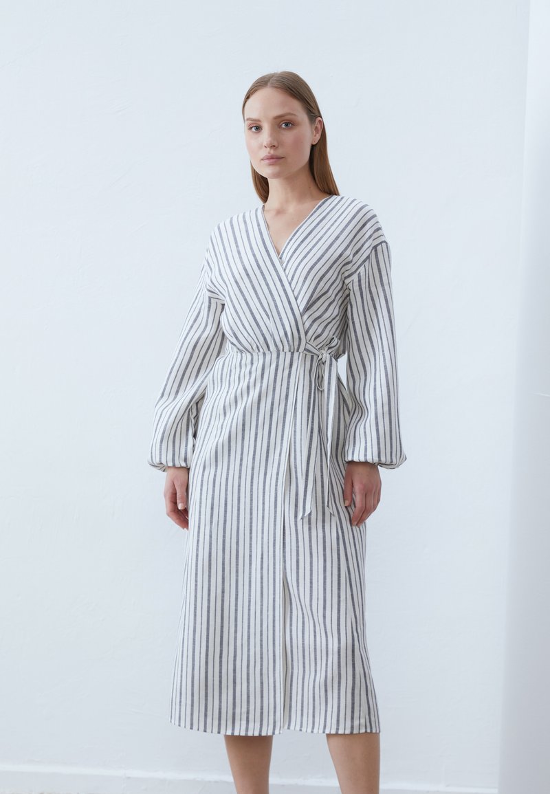 Gestreiftes, Wickelkleid aus leichtem Stoff mit langen Ärmeln. Besitzt vertikale marineblaue Streifen auf weißem Hintergrund. Inklusive einem Bindegürtel.