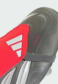 Labdarúgó cipő piros és szürke dizájnnal, texturált szintetikus anyagból, három fehér csíkkal, és szürke pánttal a biztonságos illeszkedés érdekében.