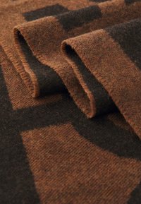 Braun- und schwarz gemusterte Decke, gefaltet, aus weicher Wolle, mit einer strukturierten Oberfläche und einem geometrischen Design.