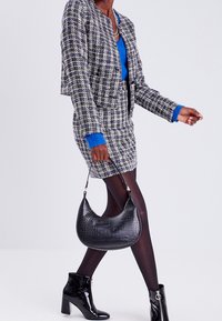Tweed blazer and skirt in black, white, and blue with a textured finish. Black crocodile-embossed handbag and shiny ankle boots.