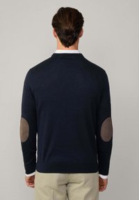 Marineblauer Pullover aus weichem Stoff mit einem gerippten Kragen und braunen Ellenbogenpatches. Er hat eine taillierte Passform und lange Ärmel.
