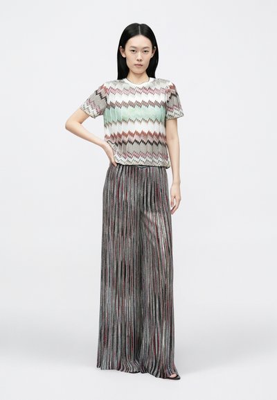 Austuots ar zigzaga rakstu pasteļtoņos, kopā ar plīsētām metāliskām platajām biksēm, radot fakturētu un slāņotu izskatu.