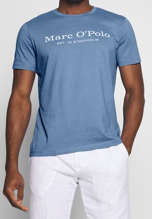 T-shirt bleu à manches courtes en mélange de coton doux, avec un texte blanc imprimé "Marc O'Polo EST. IN STOCKHOLM" sur la poitrine.