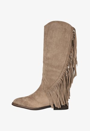 Bota alta hasta la rodilla de ante beige con flecos decorativos en el lateral, punta redonda y tacón bajo de bloque. Textura suave con un acabado uniforme.