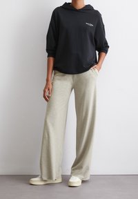 Zwarte hoodie met een losse pasvorm, gecombineerd met lichtgrijze wijde broek. Casual sneakers maken de outfit compleet.