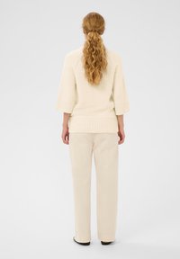 Pull en maille crème avec des manches trois-quarts et un ourlet côtelé, assorti à un pantalon beige clair, doté d'une coupe droite et d'une texture lisse.