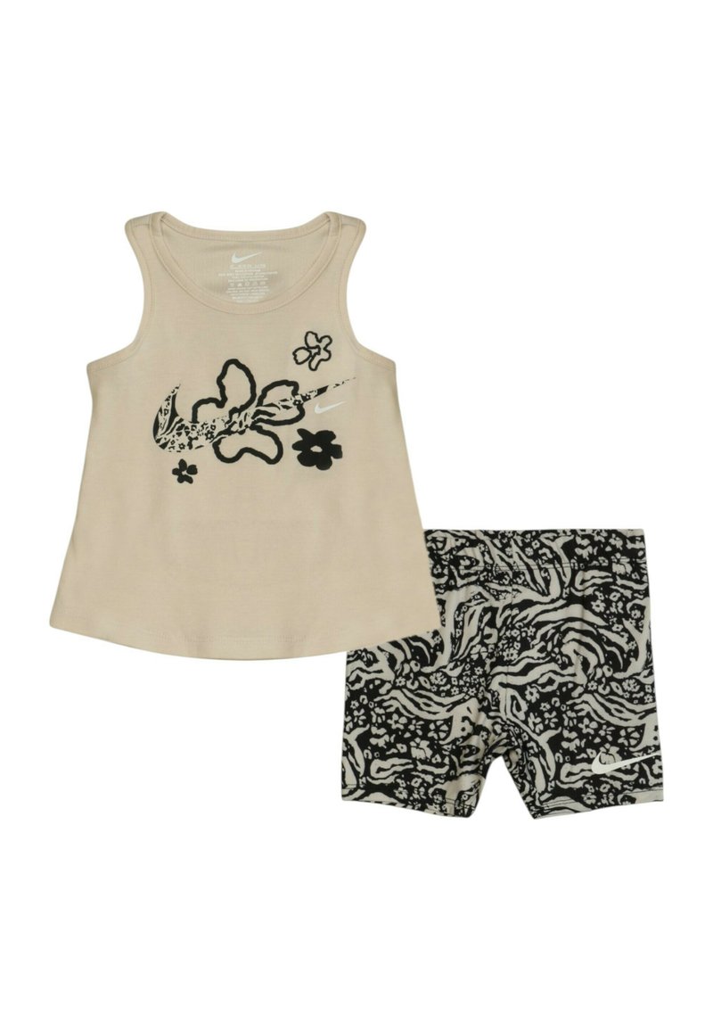 Top in cotone beige con grafiche floreali nere; abbinato a pantaloni corti a righe bianchi e neri. Tessuto morbido, design senza maniche. Adatto per un look casual.