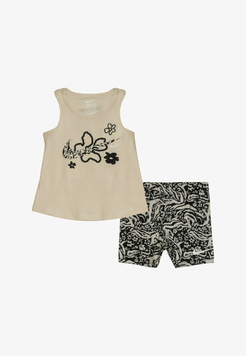 Top in cotone beige con grafiche floreali nere; abbinato a pantaloni corti a righe bianchi e neri. Tessuto morbido, design senza maniche. Adatto per un look casual.