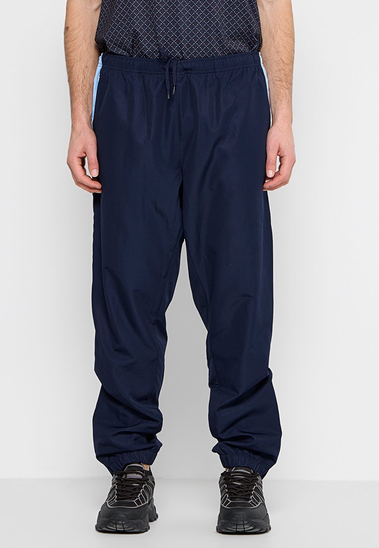 Pantalons de sport bleu marine fabriqués en matériau léger, avec une taille élastique et des poignets élastiques, dotés d'un panneau latéral de couleur bleu clair contrastant.