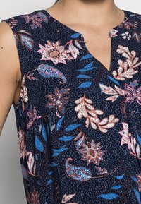 Robe sans manches en tissu bleu marine foncé présentant un motif floral et paisley en rose, blanc et bleu. Design en V avec des détails subtils.