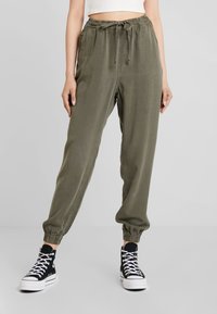 Olivgrön, lätta joggingsbyxor med elastisk midja och samlade manschetter. Matchas med svarta högskaftade sneakers.