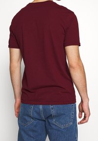 Bordeaux kortærmet t-shirt lavet af bomuld. Klassisk crew neck med oprullede ærmer, der har en glat, let tekstur.