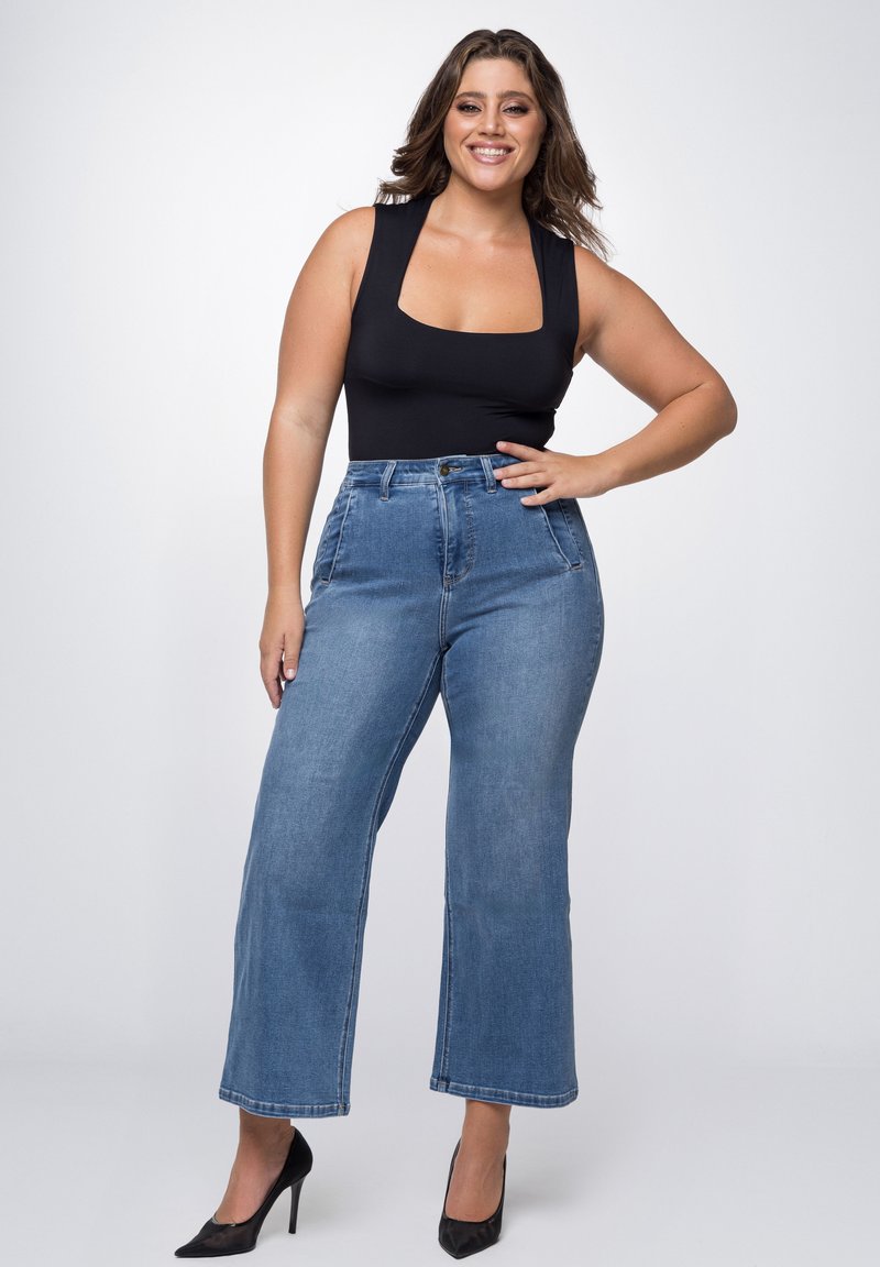 Schwarzer ärmelloser Body mit quadratischem Ausschnitt, kombiniert mit hochtaillierten blauen Denim-Weitbeinhosen und schwarzen Stilettos.