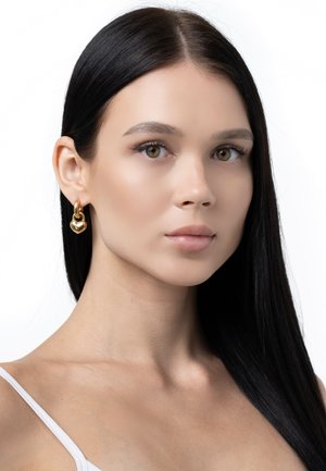 Gold hoop earrings with a heart-shaped accent, featuring a polished finish and a smooth texture, displayed on a model with straight black hair.