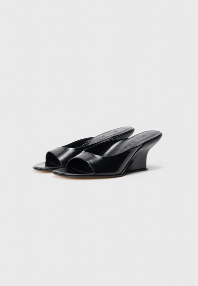 Black open-toe wedge sandals in glossy leather with a rounded shape and a smooth texture. Features a subtle platform design.