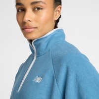 Pulover din fleece de culoare albastru deschis, cu guler înalt, dotat cu un fermoar și ornamente albe. Logo-ul New Balance în alb pe partea stângă a pieptului.