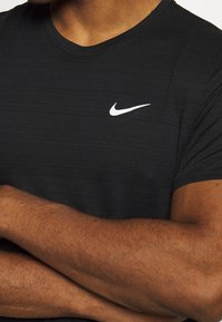 Camiseta atlética negra con cuello redondo, hecha de un tejido texturizado. Presenta un pequeño logotipo blanco de Nike en el pecho.