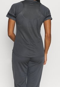 Camisa atlética gris oscuro de manga corta, con un panel de malla transpirable en la espalda. Tela suave, dobladillo redondeado y diseño minimalista.