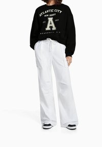 Sudadera negra con el texto "ATLANTIC CITY" y pantalones anchos blancos. Ambos tienen un ajuste casual y presentan colores contrastantes y diseños sencillos.
