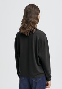 Sweat-shirt ample noir avec manches longues, encolure arrondie et texture subtile. Porté avec un jean en denim bleu.